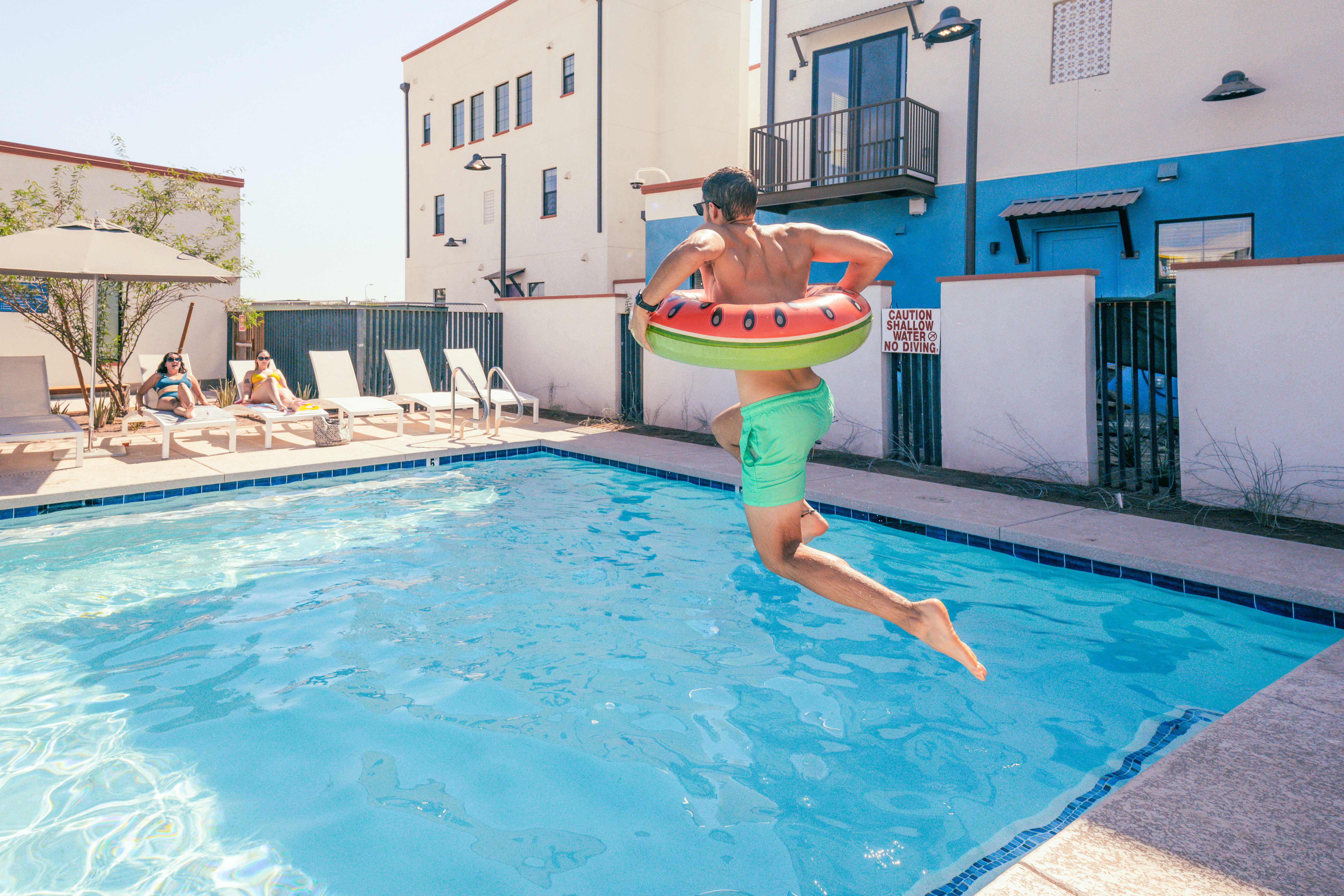 Man jumping into pool with floatie around waist