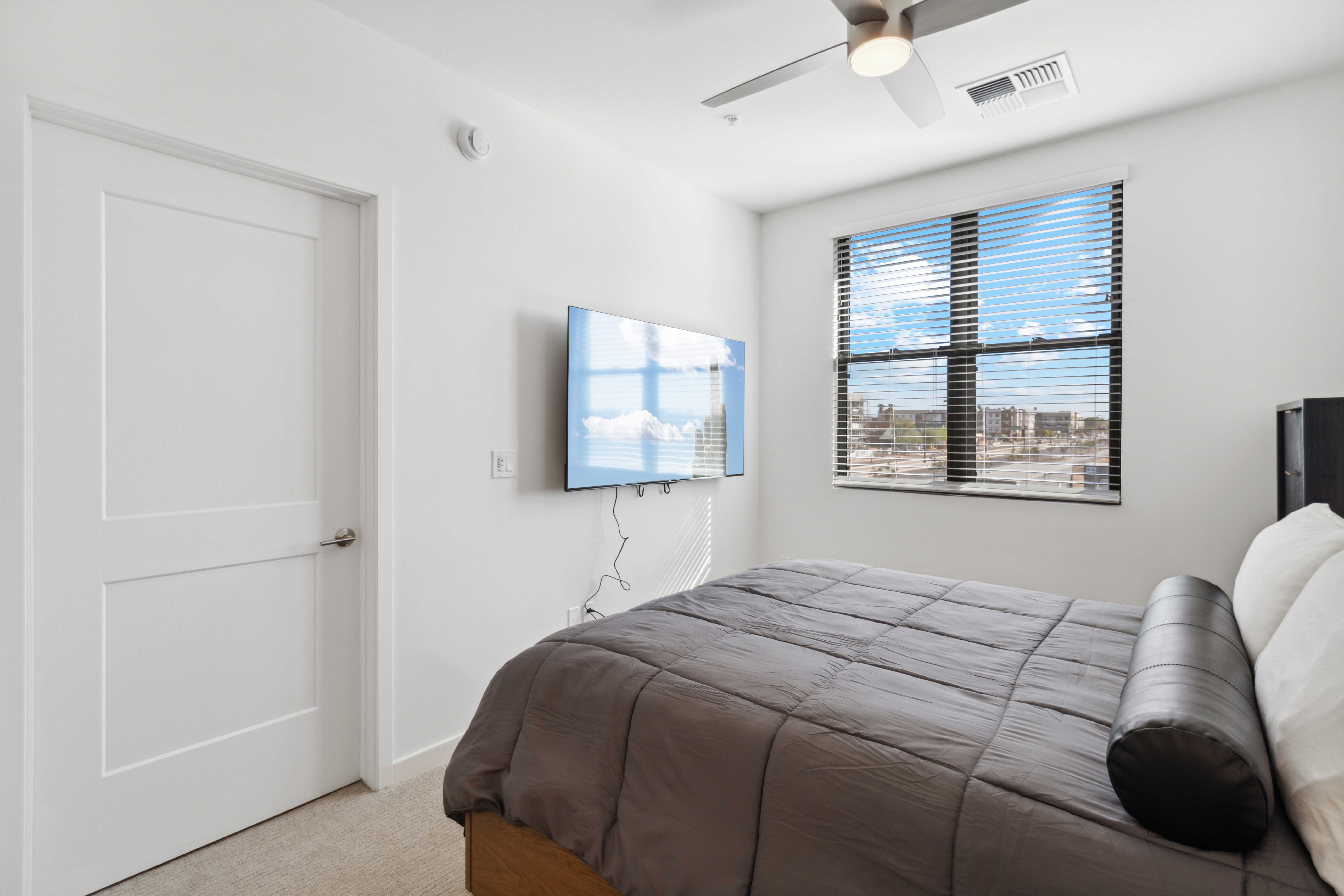 Bedroom with a wall-mounted TV, overhead fan, and large window