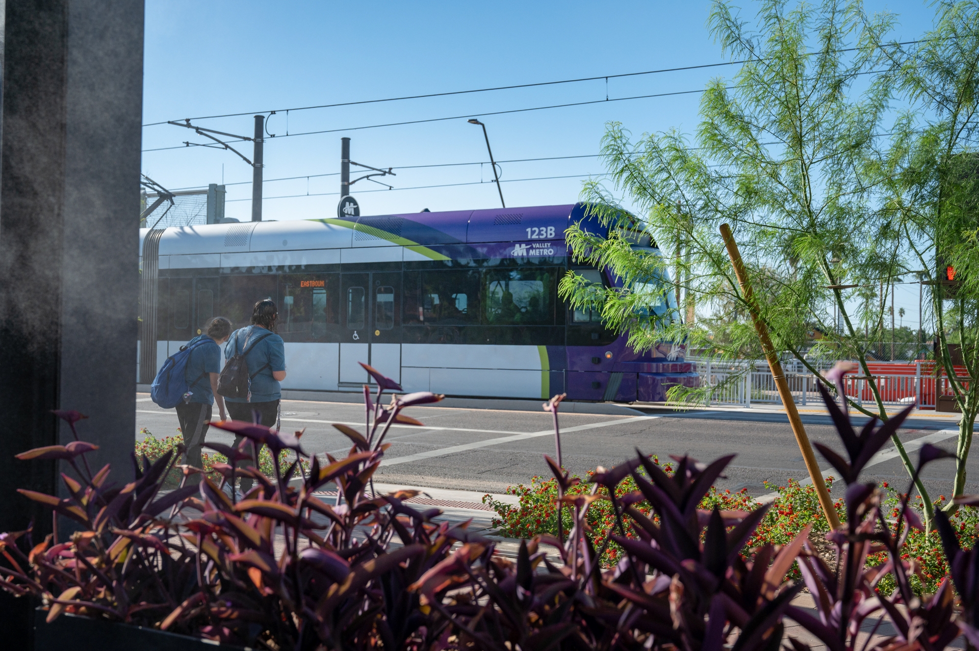 Two people about to cross the crosswalk with the Valley Metro lightrail passing in the background