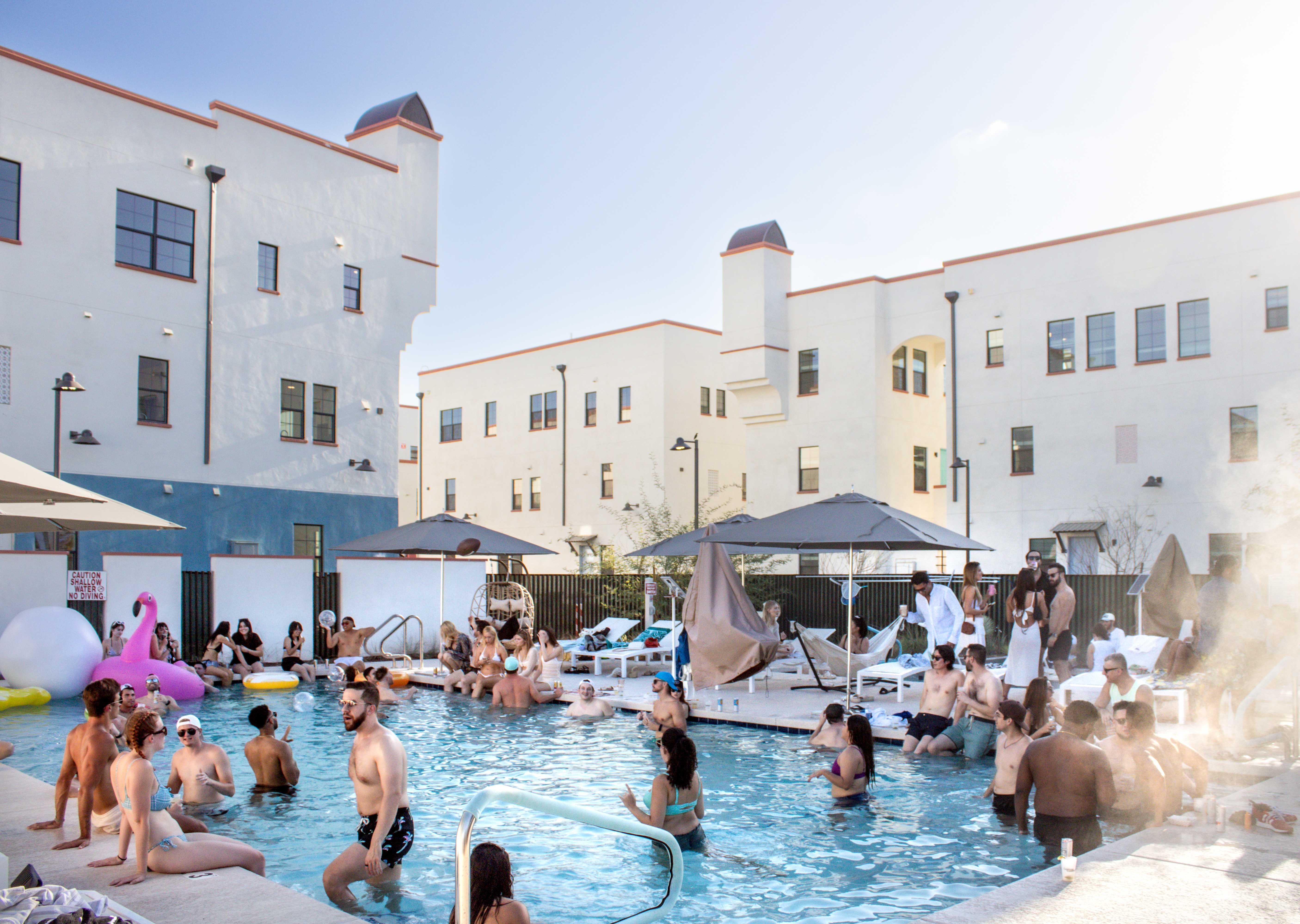 Photo of pool party with people swimming talking by lounge chairs