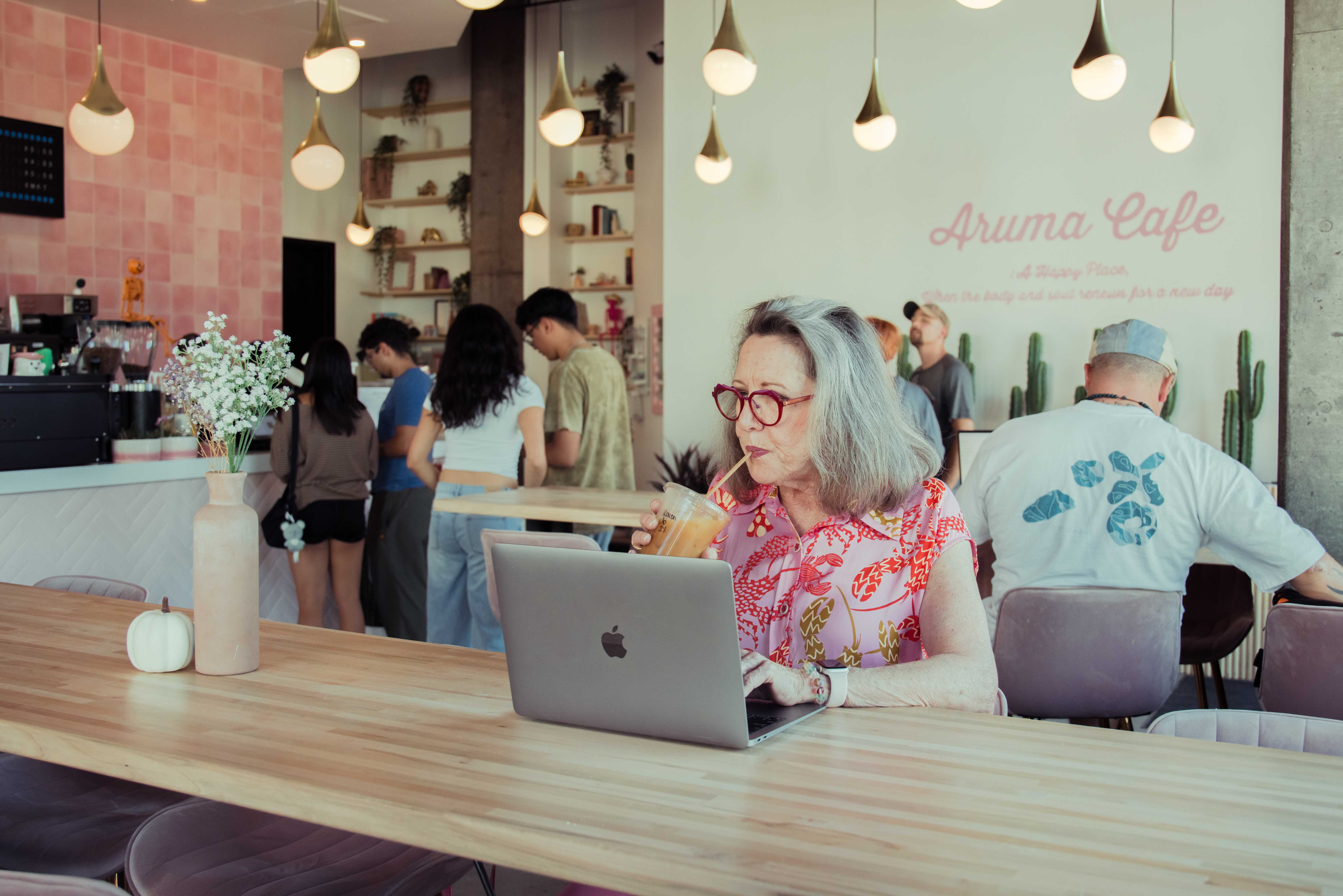 Middle-aged woman sipping iced-coffee in front of her laptop in Aruma, the coffeeshop at Culdesac