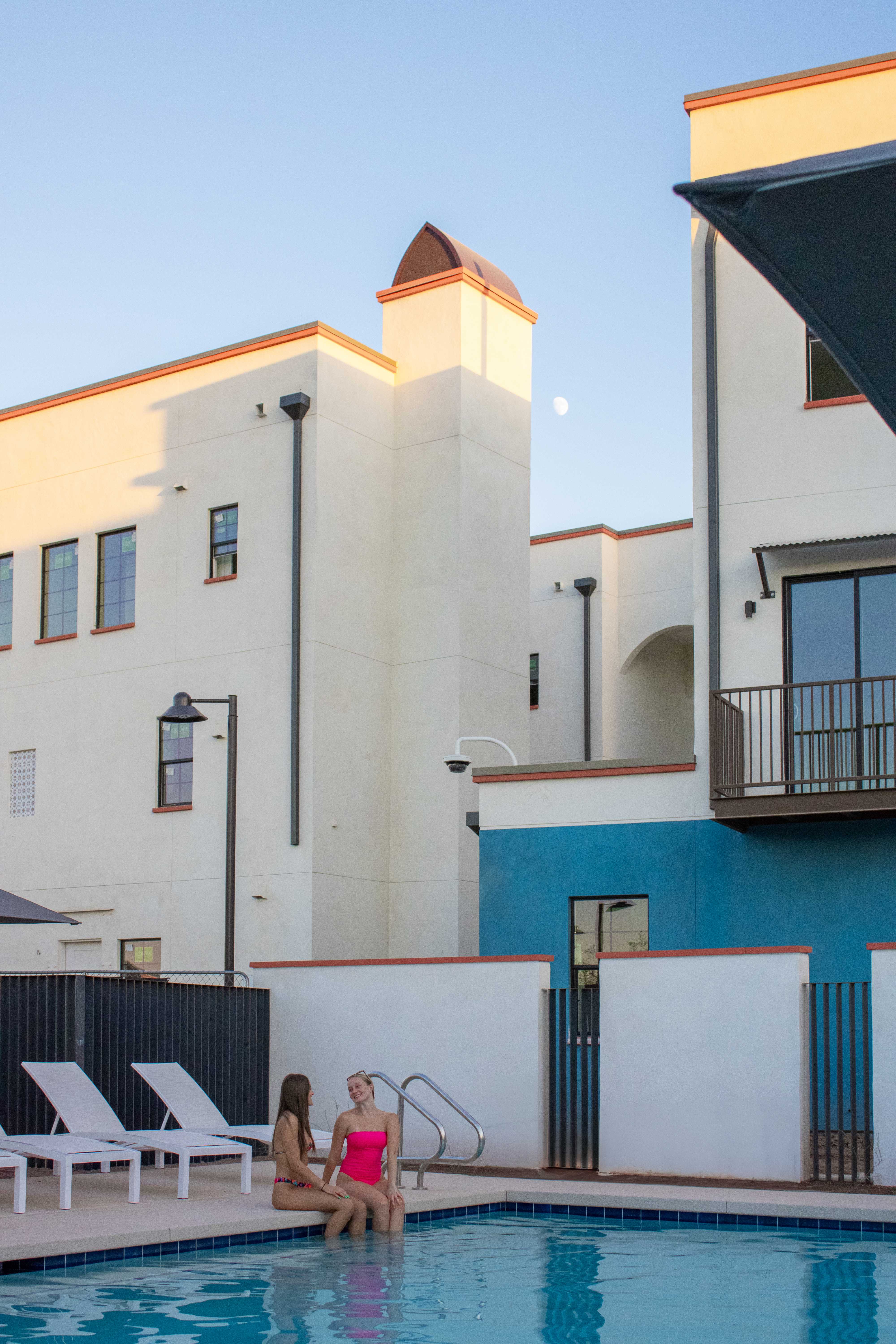 Photo of two people sitting on edge of pool with buildings in the background