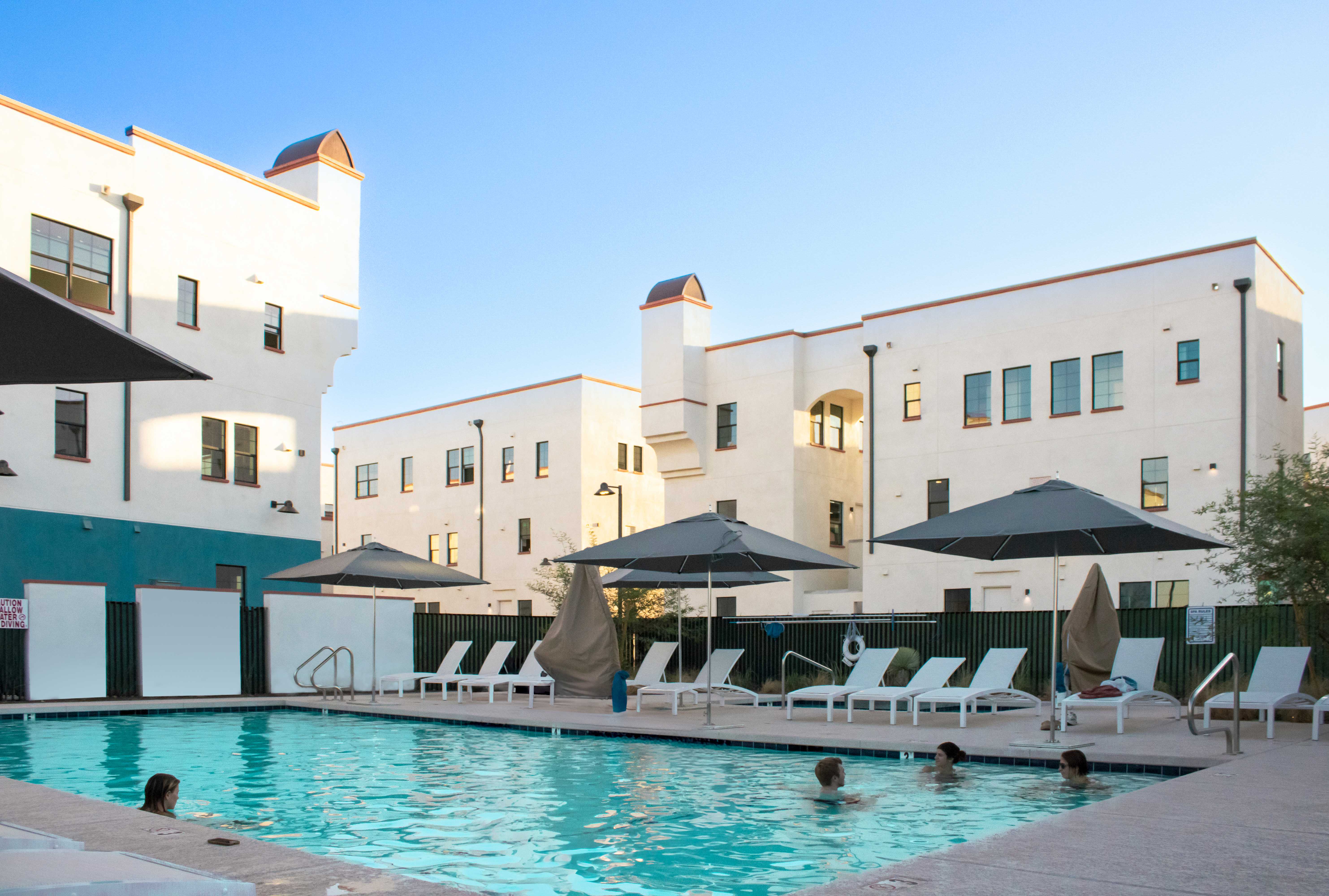 Photo of pool with people swimming and lounge chairs in the background